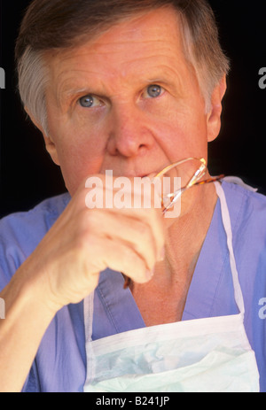 SENIOR MEDICO MASCHIO IN SCRUBS guardando pensieroso Foto Stock