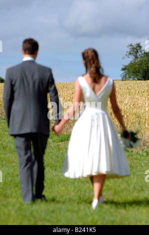 Sposi tenendo le mani a piedi lungo in un campo in una giornata di sole in Kent England Foto Stock