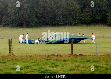 Villaggio i giocatori di cricket mettendo su copertine nella guida sotto la pioggia, Ragley Hall, Warwickshire, Inghilterra, Regno Unito Foto Stock