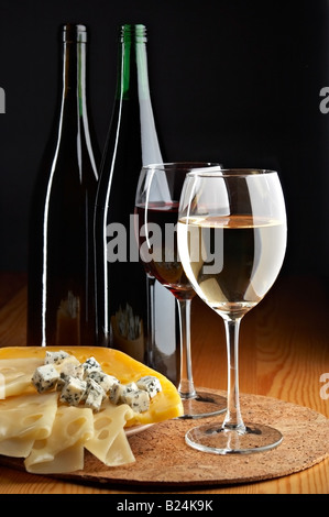 Ancora vita con formaggio vini rossi e bianchi su sfondo nero Foto Stock