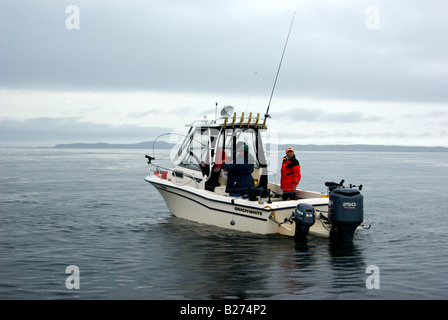 Il pescatore a bordo di un fuori bordo powered sport cruiser di fisher giocando un salmone agganciato troll pesca con downriggers Foto Stock