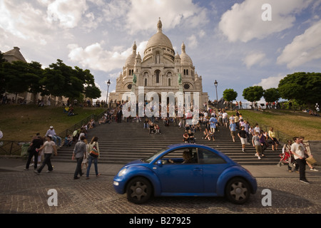 Blue Volkswagen maggiolino passando di fronte affollata scalinata che conduce alla cattedrale di Sacre Coeur e nella zona di Montmartre, Parigi Francia Foto Stock