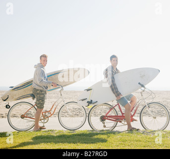 Due uomini con tavole da surf sulle biciclette Foto Stock