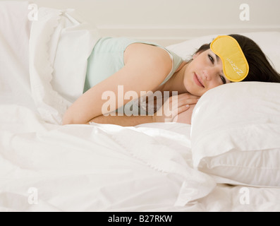 La donna posa in letto con la maschera per gli occhi Foto Stock