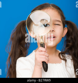 Ragazza ispanica guardando attraverso la lente di ingrandimento Foto Stock