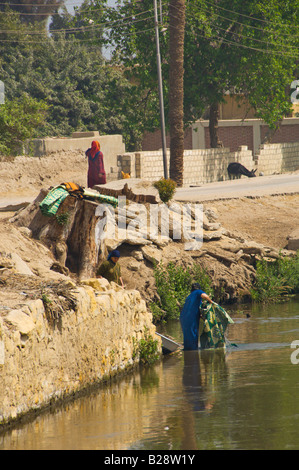 Le donne del villaggio lavare i loro vestiti e piatti in un canale di irrigazione nei pressi di El Fayoum Egitto Foto Stock