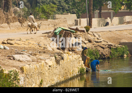 Le donne del villaggio lavare i loro vestiti e piatti in un canale di irrigazione nei pressi di El Fayoum Egitto Foto Stock