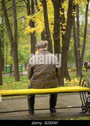 Un solitario vecchio seduto su una panchina in un parco a Mosca tra i colori d'autunno alberi Foto Stock