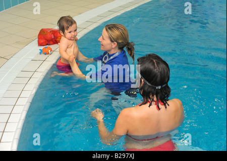 Istruttore specialista aiuta il bambino nel bagno di nuoto per la lezione di nuoto, come madre osserva Foto Stock