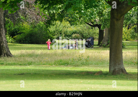 La gente nel Parco: mamma e papà rilassarsi mentre il loro bambino gioca felicemente su radure erbose. Foto Stock