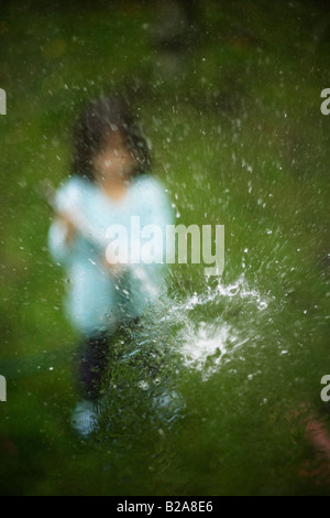 Tubo flessibile spruzzata in una finestra di vetro bambina di cinque anni razza mista indiano caucasico etnica Foto Stock