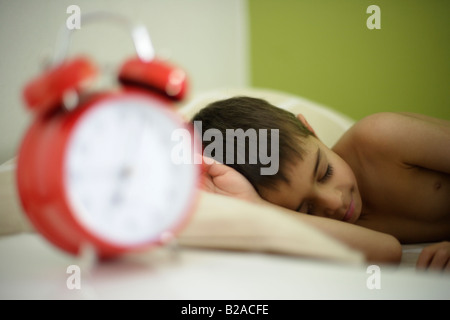 Ragazzo di età compresa tra i sei posti letto nel suo letto accanto a Colore rosso brillante sveglia razza mista inglese indiano Foto Stock