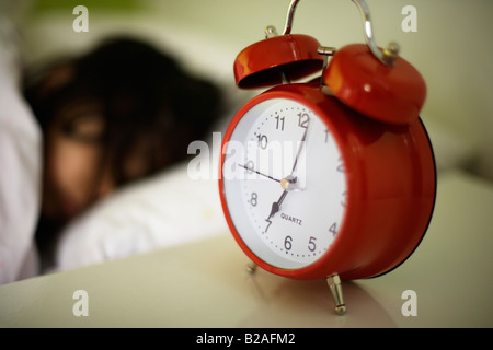 Ragazza di età compresa tra i cinque posti letto nel suo letto accanto a Colore rosso brillante sveglia razza mista inglese indiano Foto Stock