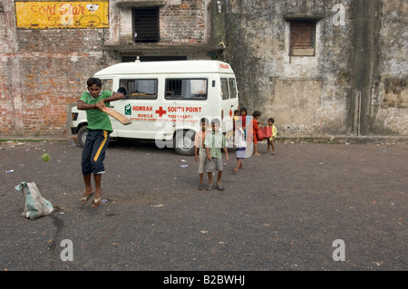 Come il cricket è l'indiano sport nazionale, i bambini e i ragazzi giocare ovunque, in questo caso nella parte anteriore di una ambulanza belon Foto Stock