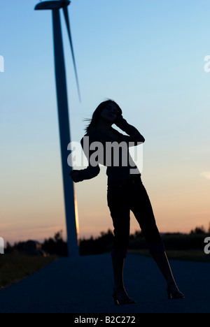 Silhouette giovane donna in piedi su una strada con il mulino a vento Foto Stock