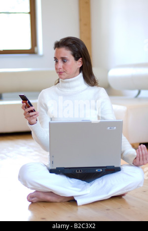 Giovane donna pratica dello yoga con un notebook sul grembo e telefonare Foto Stock