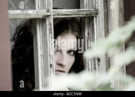 Giovane donna che guarda fuori da una finestra longingly Foto Stock