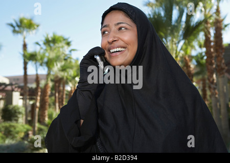 Donna musulmana in nero hijab parlando al cellulare, ridendo Foto Stock