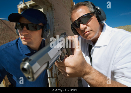 Istruttore assiste l uomo mirando a pistola al poligono di tiro Foto Stock