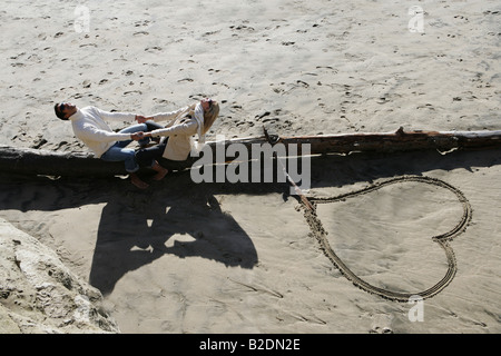 Coppia giovane tenendo le mani sul log in spiaggia. Foto Stock