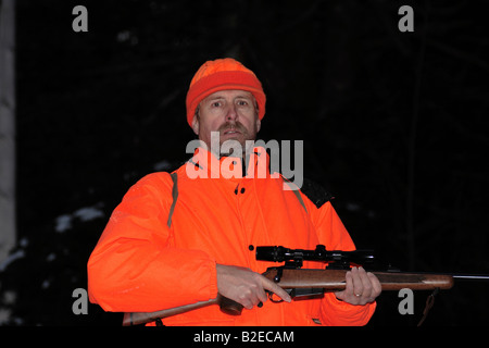 Un cacciatore dei cervi in hunter orange abbigliamento tenendo un alto powered rifle Foto Stock