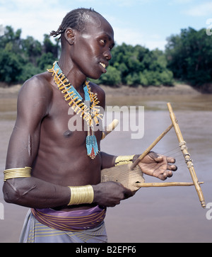 Un Karo uomo con capelli intrecciati svolge un tradizionale strumento a corda accanto al fiume Omo vicino Duss. Foto Stock