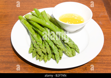 I germogli di asparagi e il burro dip su una porcellana bianca piastra. Foto Stock