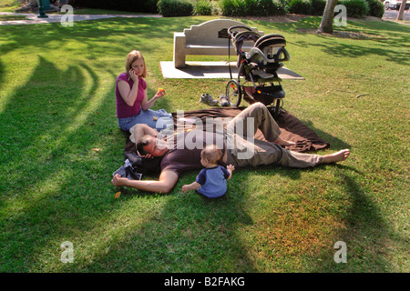 Un padre ammira il suo neonato mentre sua moglie chat su un telefono cellulare all'aperto su un pomeriggio estivo a Coronado CA Foto Stock