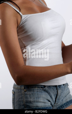 Giovani sinuosa donna africana indossando un bianco strappy top e gli shorts in denim blu afro-caraibica curva voluttuoso marrone della pelle Foto Stock