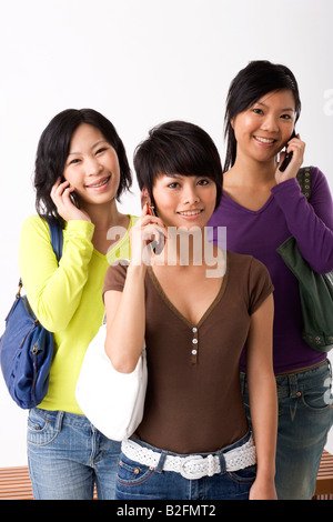 Ritratto di tre giovani donne di parlare su telefoni cellulari e sorridente Foto Stock