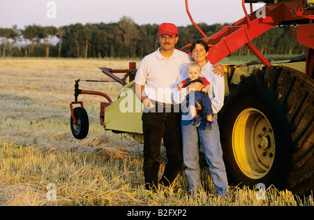 Famiglia giovane in piedi accanto a una mietitrebbia in un campo Foto Stock