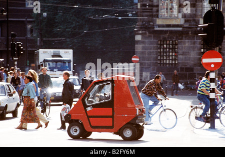 Piccola auto guidando attraverso il centro di amsterdam passato i pedoni e i ciclisti Foto Stock