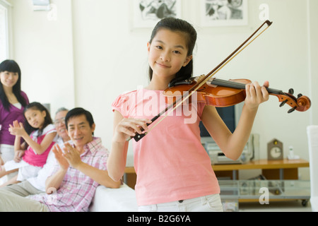 Ragazza che gioca un violino con la sua famiglia ad applaudire in background Foto Stock