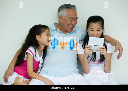 Ragazza che gioca con un palmare video gioco accanto a suo nonno e sorella Foto Stock