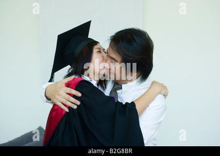Profilo laterale di una metà femmina adulta graduate abbracciando e baciando il marito Foto Stock