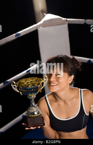 Giovane donna tenendo un trofeo e sorridente in un anello di inscatolamento Foto Stock