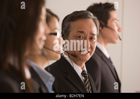 Ritratto di un imprenditore che indossa un auricolare con due imprenditrici e di imprenditore accanto a lui Foto Stock