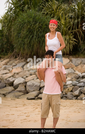 Giovane donna seduta su un giovane di spalle sulla spiaggia Foto Stock