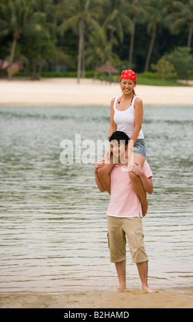 Giovane donna seduta su un giovane di spalle sulla spiaggia Foto Stock