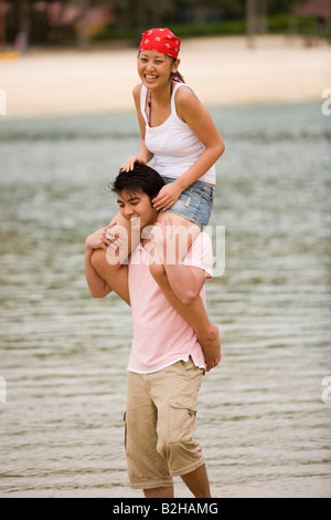 Giovane donna seduta su un giovane di spalle sulla spiaggia Foto Stock