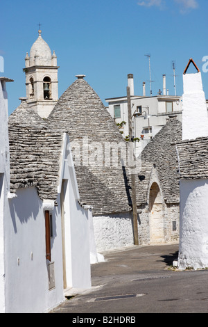 Gruppo di Trulli case con il campanile di una chiesa e di moderni appartamenti in background,Alberobello,Puglia,Italia Foto Stock