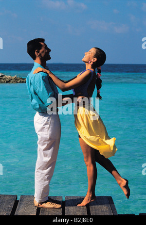 Maldive. Vista laterale della romantica coppia giovane in piedi sul fronte oceano, pontile in legno. Foto Stock