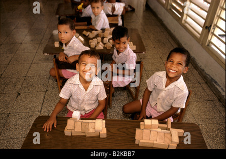 Scuola sorridente i ragazzi alle loro scrivanie giocando con la costruzione in legno di blocchi in Cuba Foto Stock