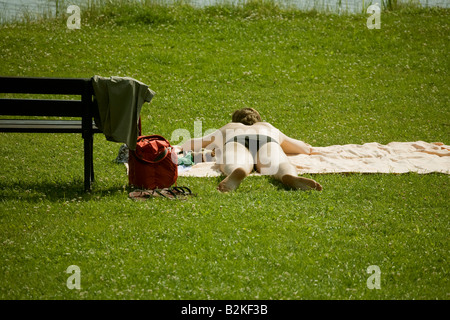 Un giovane uomo sunbathes su un prato da un lago Foto Stock