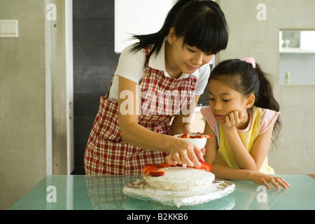 Metà donna adulta decorare la torta con fette di fragola Foto Stock