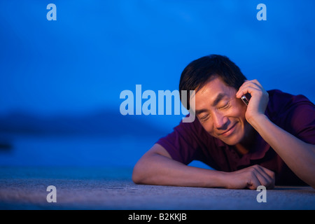 Metà uomo adulto che giace sulla spiaggia e a parlare su un telefono mobile Foto Stock