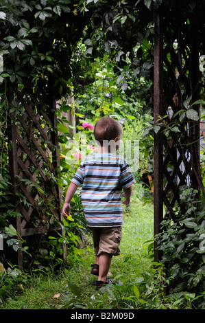 Un ragazzo a piedi attraverso un pergolato in un giardino incantato Foto Stock