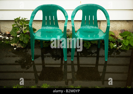 Due bambini piccoli s plastica sedie da giardino in piedi in una pozzanghera accanto a una casa weatherboard Foto Stock