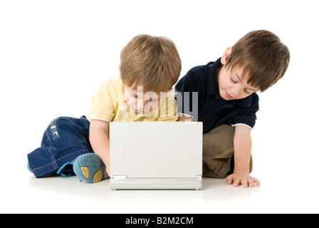 Due bambini che giocano con il laptop seduto sul pavimento Foto Stock