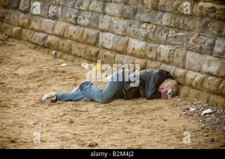 Uomo caucasico maturo vestito casualmente con jeans e giacca in pelle addormentato sulla spiaggia di Scarborough. North Yorkshire. REGNO UNITO. Foto Stock